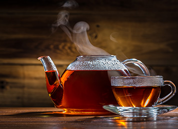 Hot tea in a kettle with cup next to a lemonand mint